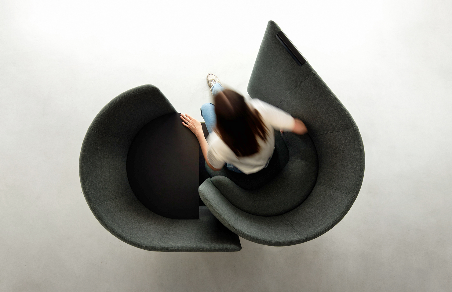 Person sitting in a modern, swivel work pod on a plain background