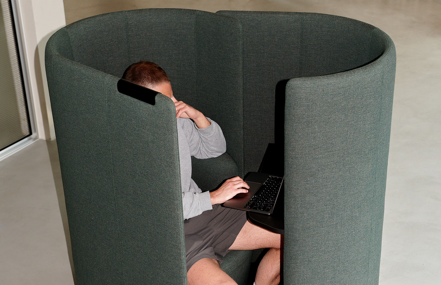 Person using a laptop inside a cylindrical green fabric work pod.