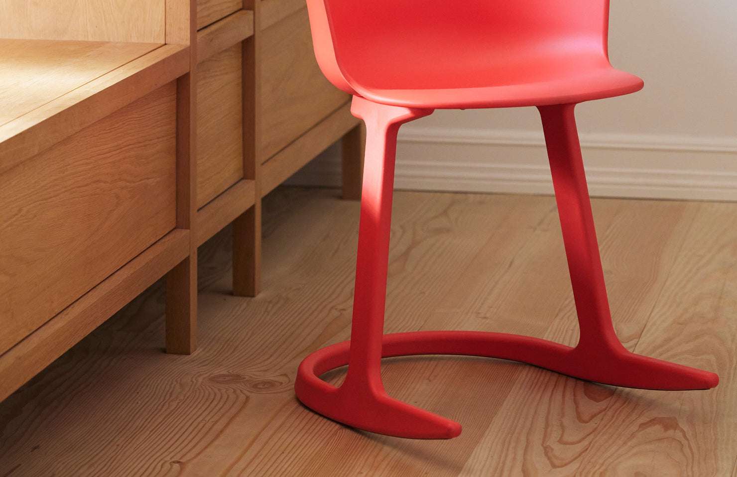 Red chair with a unique design on a wooden floor next to wooden furniture.