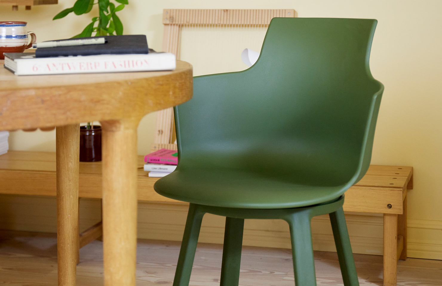 Green turn chair in front of a wooden table with books and a plant in a room.