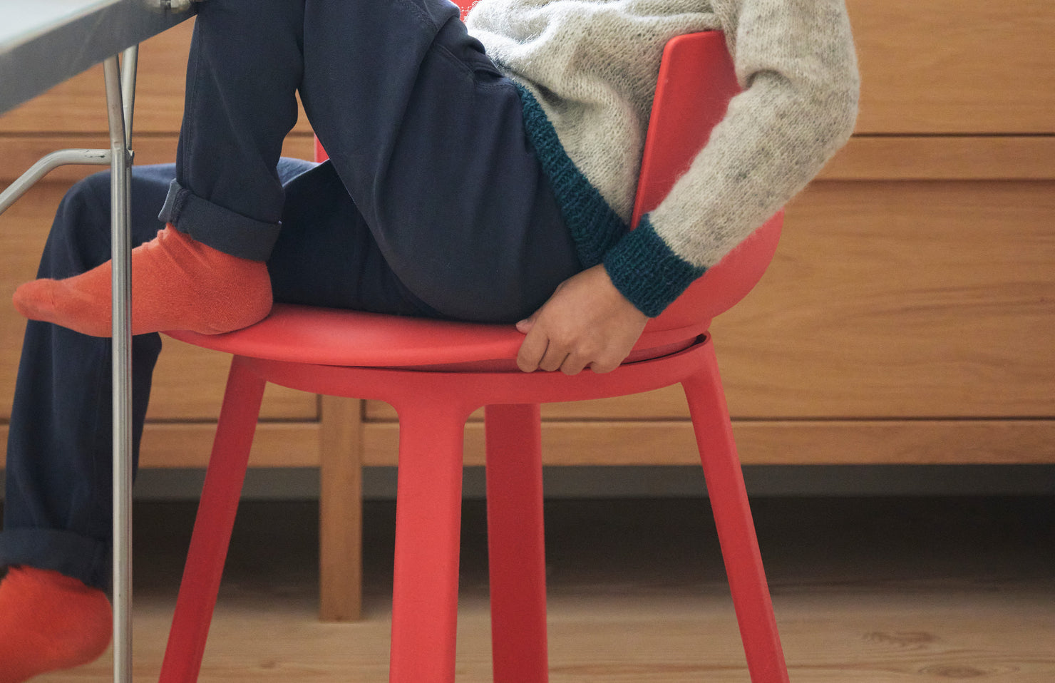Person sitting on a red turn chair with a wooden floor and wall in the background