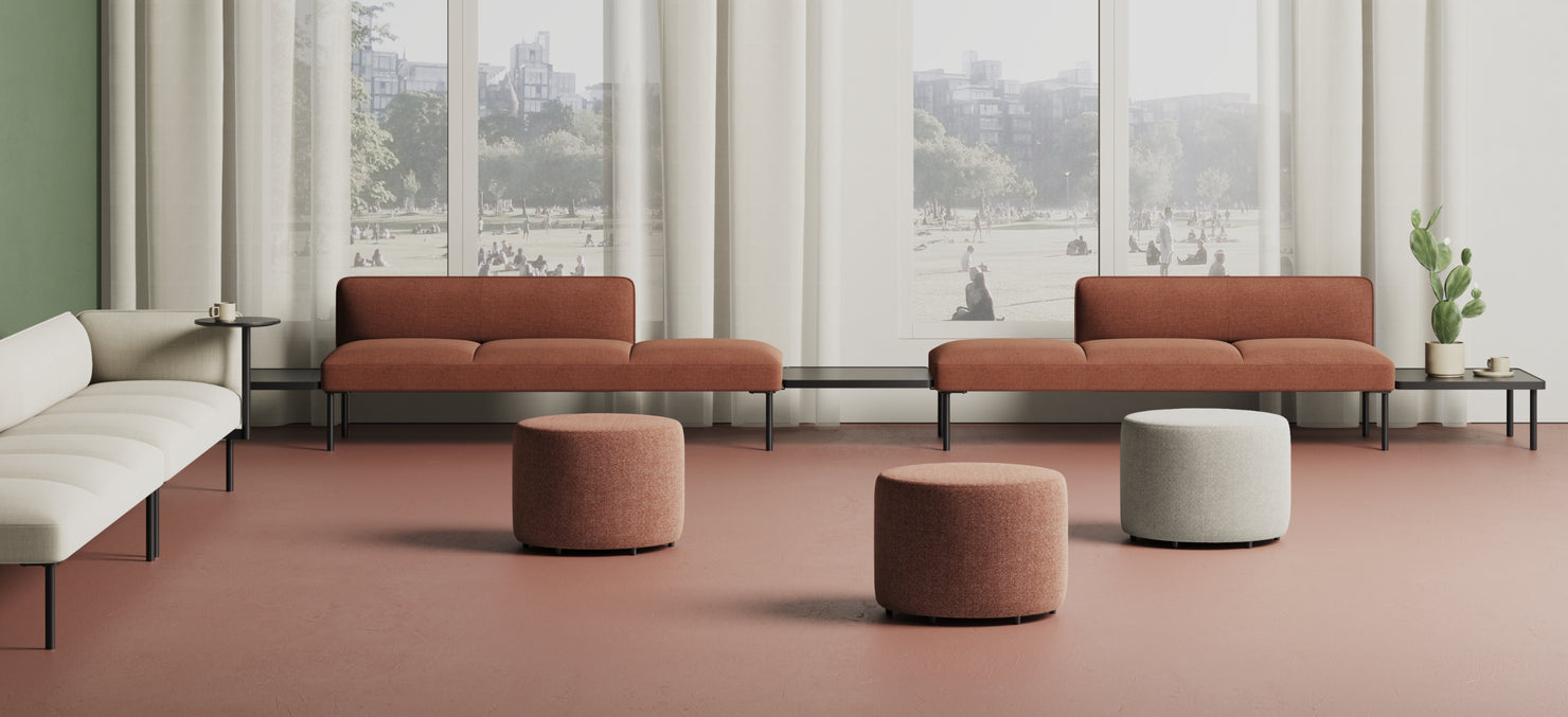 Adapt Modular Seating in rust color paired with Breck Tables, set in a bright lounge space with large windows and greenery outside.