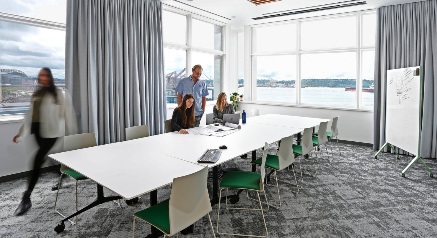Cushing Terrel's modern workspace with people working around a a large, white conference table, featuring Ocee and Four Design's white FourCast2 Stackers with green seatpads.