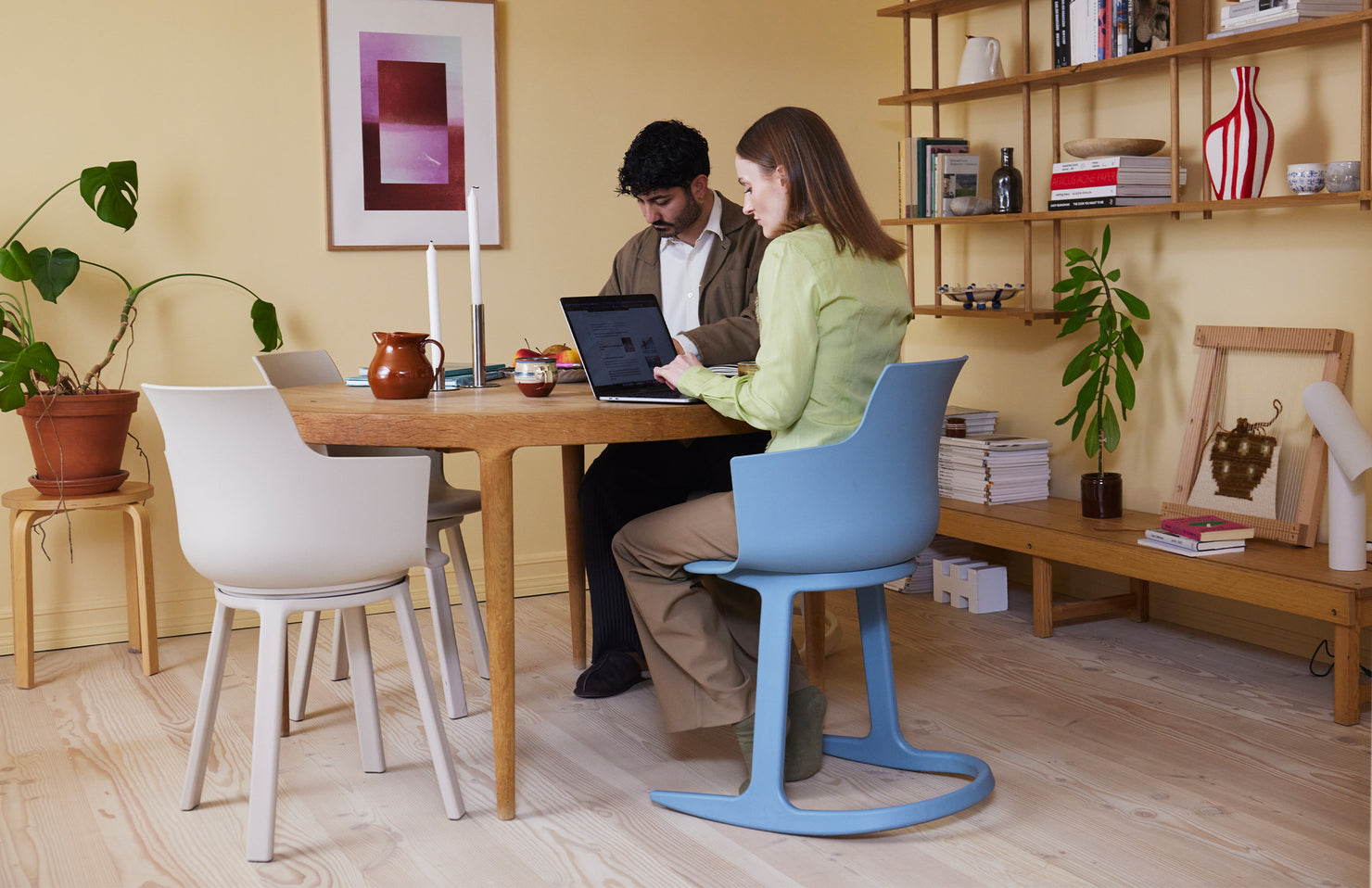 Two people sitting at a wooden table with a laptop, one person in a blue tilt chair, surrounded by office decor elements.