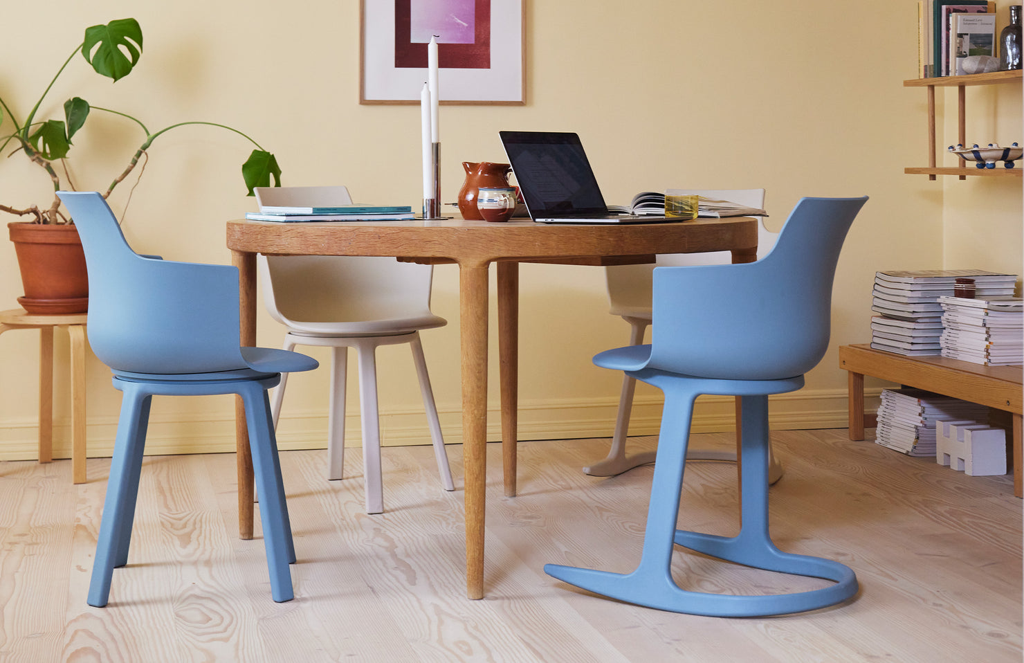 Blue and cream chairs around a wooden table in a work room with a plant and shelves.